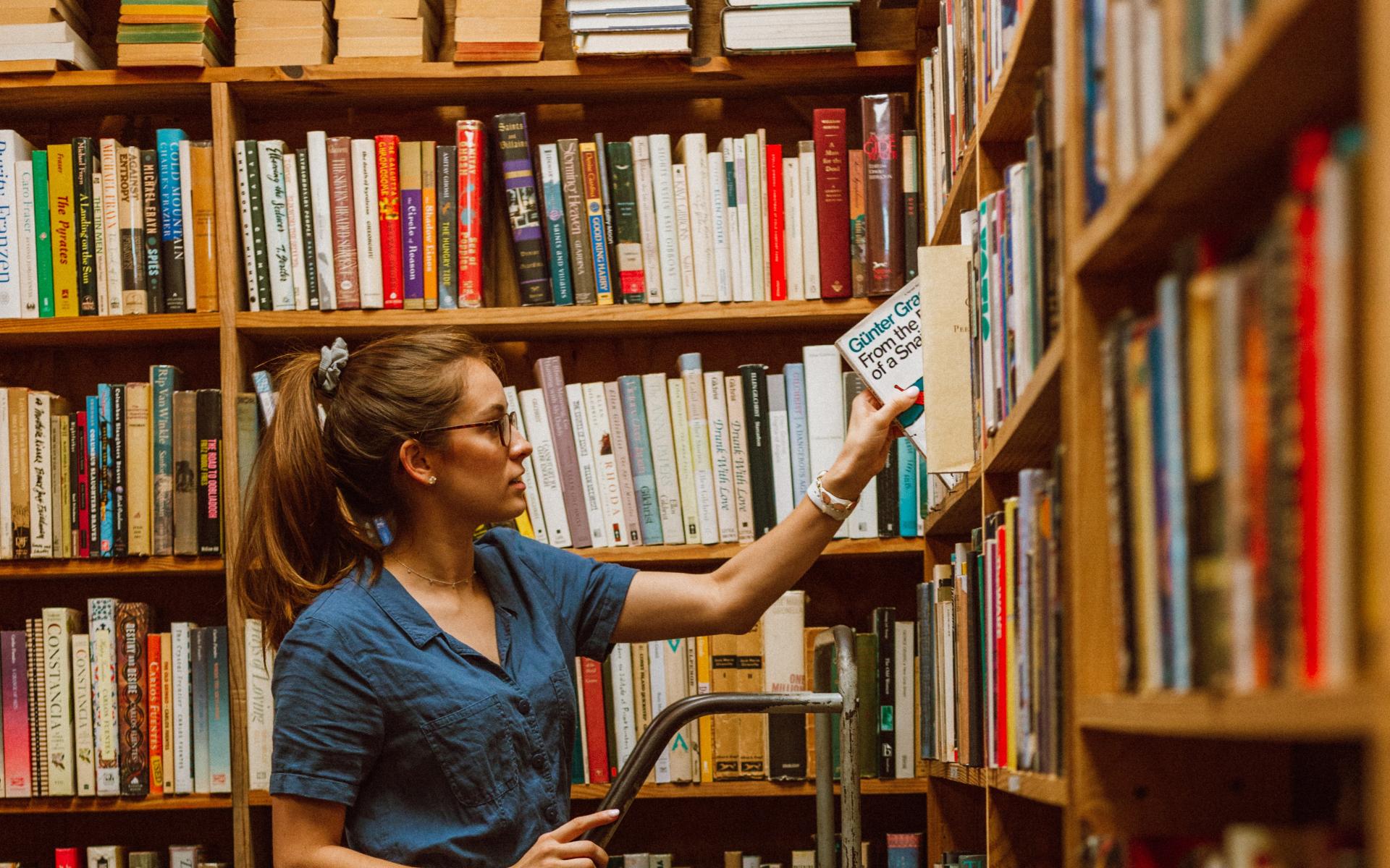 Junge Frau auf einer Leiter vor dem Bücherregal